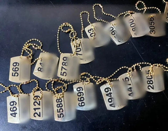 Brass dog tags on ball chains with engraved numbers, names hidden